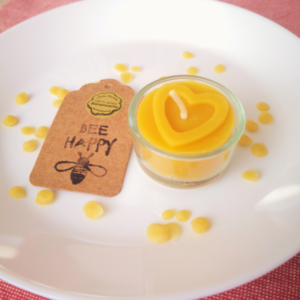 Bienenwachskerze in Teelichtgröße mit Herzmotiv in einem Glas; dekoriert mit Bienenwachskugeln auf einem Teller; HofladenBOX