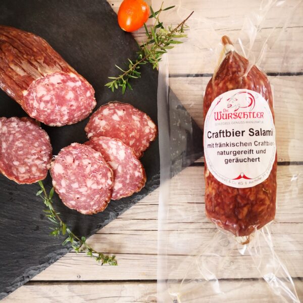 Craftbier Salami im Ganzen und aufgeschnitten auf einer Schieferplatte angerichtet und mit Kräutern garniert; HofladenBOX